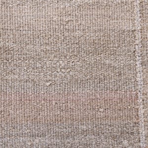 Pu&ograve; includere: Primo piano di un tappeto beige tessuto con una texture sottile. Il tappeto presenta una striscia leggermente pi&ugrave; scura che attraversa orizzontalmente il centro.
