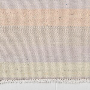 K&ouml;nnte beinhalten: Ein gewebter Teppich mit einem gestreiften Muster in Hellrosa, Creme und Hellgrau. Der Teppich hat einen Fransenrand.
