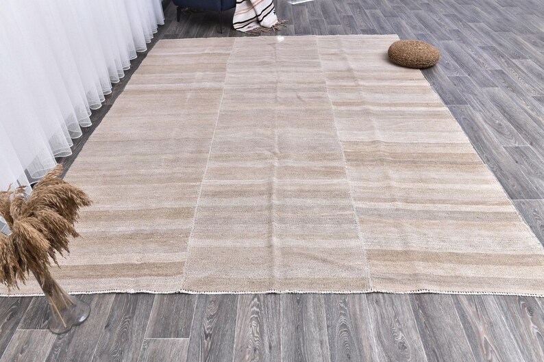 Pu&ograve; includere: Un tappeto beige chiaro con un sottile motivo a righe. Il tappeto ha una trama tessuta e un bordo con frange.