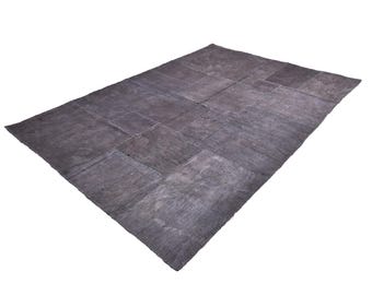Può includere: Un tappeto grigio a patchwork di forma rettangolare. Il tappeto è composto da diversi pezzi di tessuto cuciti insieme.