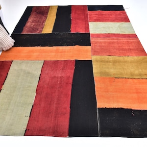 May include: A rectangular area rug featuring a patchwork design of large, solid-colored blocks in black, red, orange, yellow, and muted green. The sections are joined with visible stitching, creating a grid-like pattern across the entire surface.