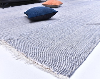 May include: A woven area rug with a blue and white striped pattern. The rug has a fringed edge and is paired with two decorative pillows, one blue and one orange.