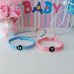 May include: Two friendship bracelets, one blue and one pink, with the letters "H" and "T" on the charms.