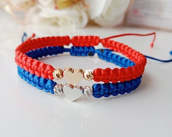 May include: Two friendship bracelets with red and blue cords, featuring a gold and silver heart charm.