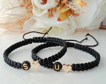 May include: Two black friendship bracelets with gold heart charms and letter beads spelling "S" and "U".