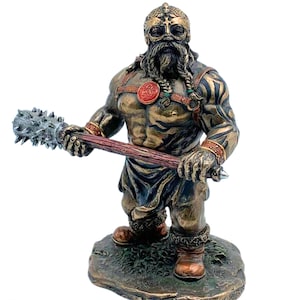 Peut inclure: Une statue en bronze d'un guerrier viking tenant une massue à pointes. Le guerrier porte un casque à cornes, une jupe en cuir et une cotte de mailles. Il a une longue barbe et des tatouages sur les bras.