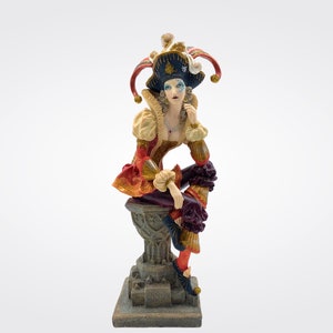 May include: A figurine of a jester wearing a red, gold, and black costume with a blue and gold hat. The jester is sitting on a stone pedestal with a thoughtful expression.