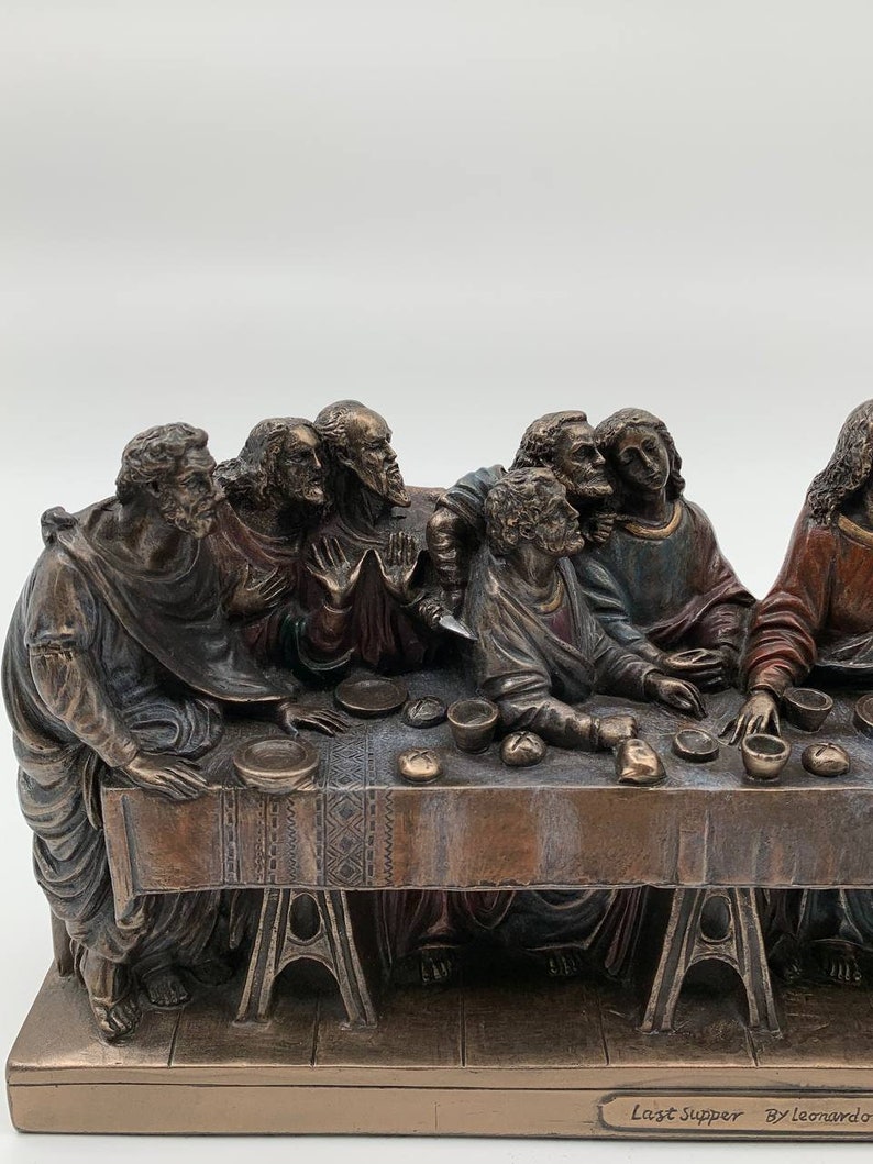 May include: A bronze sculpture depicting Leonardo da Vinci's The Last Supper. The sculpture features 13 figures seated around a table, with Jesus Christ in the center. The sculpture is detailed and realistic, with intricate facial expressions and clothing folds. The base of the sculpture is inscribed with "Last Supper By Leonardo."
