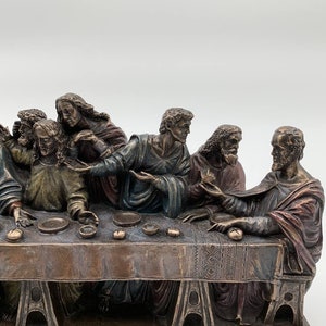 May include: A bronze sculpture depicting the Last Supper, featuring Jesus and his disciples seated around a table. The sculpture is detailed with realistic facial expressions and clothing. The base of the sculpture is inscribed with "Santa delle Grazie Church."