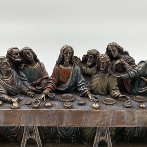 May include: A bronze sculpture depicting Leonardo da Vinci's Last Supper, featuring 13 figures seated around a table. The sculpture is a detailed replica of the famous fresco in the Santa Maria delle Grazie church in Milan, Italy. The inscription on the base reads "Last Supper by Leonardo da Vinci The S. Maria delle Grazie Church".