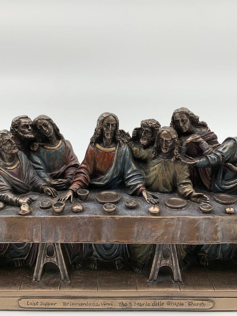 May include: A bronze sculpture depicting Leonardo da Vinci's Last Supper, featuring 13 figures seated around a table. The sculpture is a detailed replica of the famous fresco in the Santa Maria delle Grazie church in Milan, Italy. The inscription on the base reads "Last Supper by Leonardo da Vinci The S. Maria delle Grazie Church".