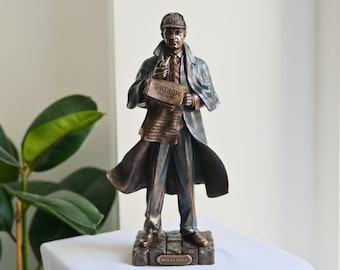 May include: A bronze-colored Sherlock Holmes statue, wearing a hat and coat, holding a newspaper with the headline "Hastily Murder". The statue is on a stone-like base, with the name "Sherlock Holmes" inscribed.