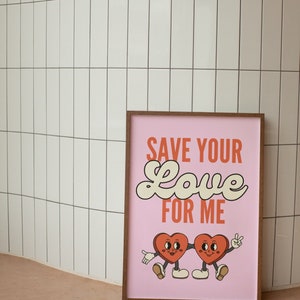 May include: A pink framed print with the text "SAVE YOUR LOVE FOR ME" in white and orange lettering. Two cartoon hearts with legs and faces are holding hands.