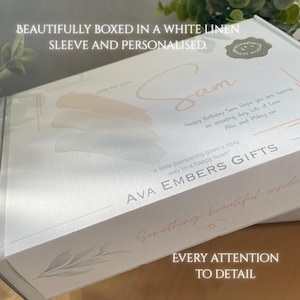 May include: A white gift box with a linen texture, personalized with the name "Sam" in a soft pink script. The box includes the text "AVA EMBERS GIFTS" and the phrase "Something beautiful inside."