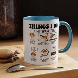 May include: White ceramic mug with a blue rim and handle. The mug features a graphic of a beagle dog and the text "THINGS I DO IN MY SPARE TIME". The graphic shows a beagle dog in different activities, including looking at a beagle, watching beagle videos, researching beagle, talking about beagle, thinking about beagle, and dreaming about beagle.