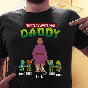 May include: Black t-shirt with a green and red "TURTLEY AWESOME DADDY" graphic. The graphic features a purple cat character with four Teenage Mutant Ninja Turtles characters. The text "NAME NAME DAD NAME NAME" is below the characters.