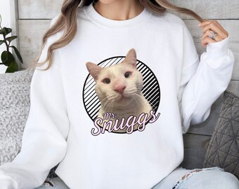 May include: White sweatshirt with a black and white circle graphic featuring a white cat with blue eyes. The text "Mr. Snuggs" is written in pink cursive below the cat.