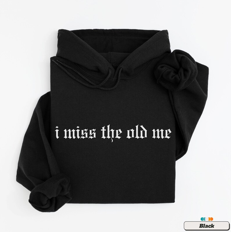 Puede incluir: Sudadera con capucha negra con el texto "i miss the old me" en fuente g&oacute;tica blanca.