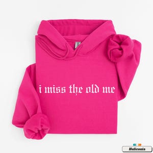 Puede incluir: Una sudadera con capucha rosa con un gr&aacute;fico blanco que dice "i miss the old me" en una fuente g&oacute;tica.