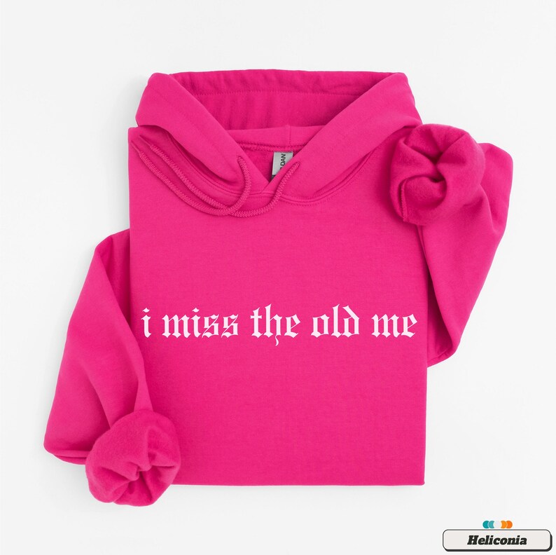 Puede incluir: Una sudadera con capucha rosa con un gr&aacute;fico blanco que dice "i miss the old me" en una fuente g&oacute;tica.