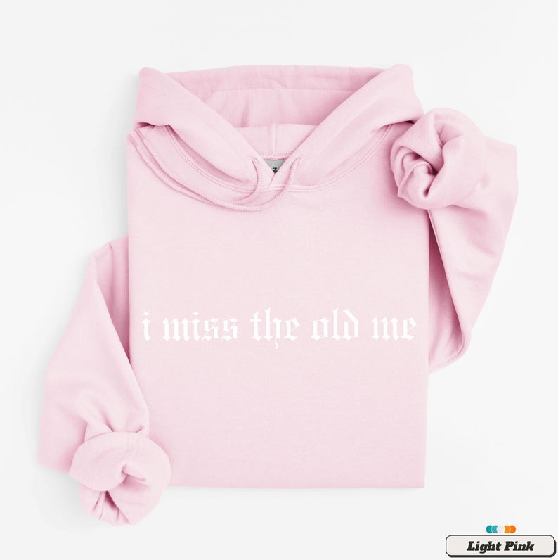 Puede incluir: Sudadera con capucha rosa claro con el texto "i miss the old me" en blanco.