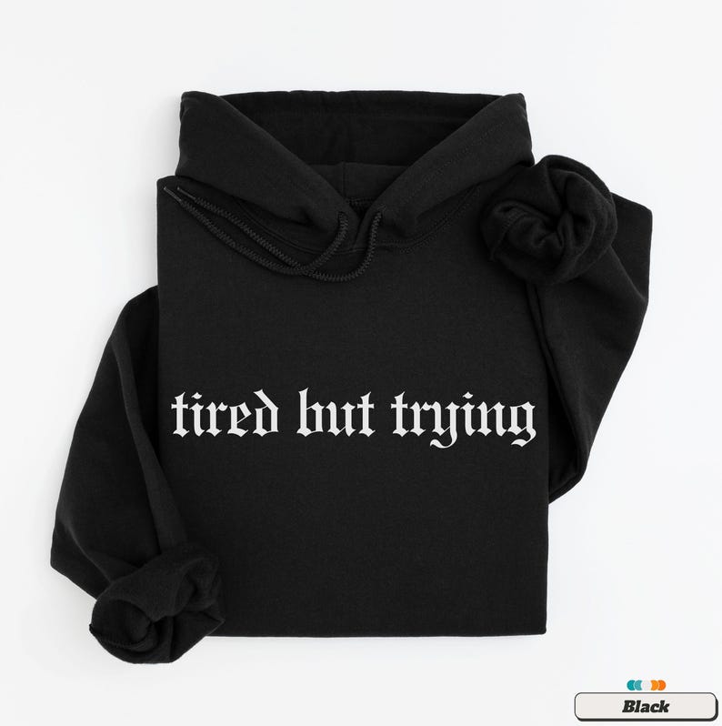 May include: Black hooded sweatshirt with the text "tired but trying" in white gothic font.