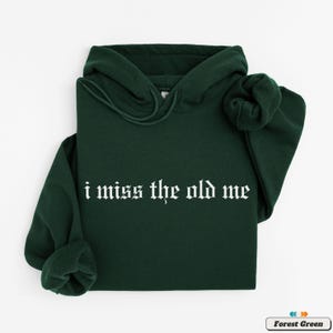 Puede incluir: Una sudadera con capucha de color verde bosque con el texto "i miss the old me" en fuente g&oacute;tica blanca.