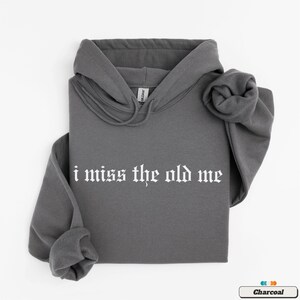 Puede incluir: Una sudadera con capucha de color gris carb&oacute;n con el texto "i miss the old me" impreso en blanco en la parte delantera.