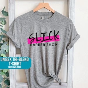 May include: Gray unisex tri-blend t-shirt with the text "SLICK BARBER SHOP" in black lettering with a pink stripe underneath.