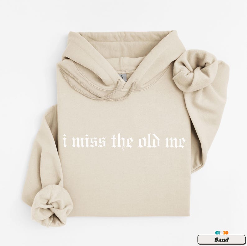 Puede incluir: Una sudadera con capucha de color arena con un cord&oacute;n blanco y el texto "i miss the old me" impreso en blanco en la parte delantera.