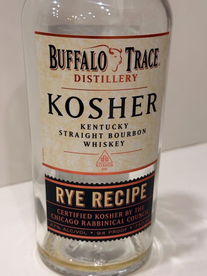 K&ouml;nnte beinhalten: Eine klare Glasflasche Buffalo Trace Kosher Rye Recipe Whiskey. Das Etikett zeigt den Namen der Brennerei, Produktdetails und Zertifizierungsinformationen. Das Etikett ist cremefarben und schwarz mit roten Akzenten. Die Flasche enth&auml;lt 750 ml Whiskey.