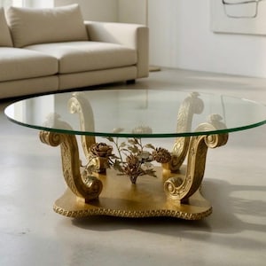 May include: A round coffee table with a clear glass top and ornate gold-colored base. The base features scrolled details and a decorative floral arrangement. The table is a statement piece for a living room.