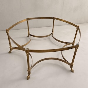 May include: A brass coffee table frame featuring a circular top support connected by four vertical legs. Each leg is detailed with a slender, turned post design and terminates in a small, claw-style foot. The structure is open and metallic.