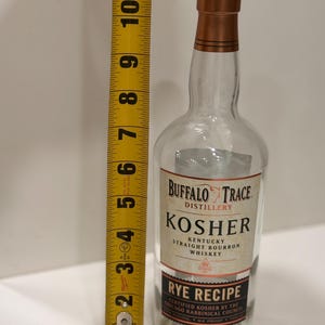 K&ouml;nnte beinhalten: Eine klare Glasflasche Buffalo Trace Kosher Kentucky Straight Bourbon Whiskey. Die Flasche ist etwa 25 cm hoch, mit einem schwarzen Verschluss und einer kupferfarbenen Halsmanschette. Das Etikett lautet "Rye Recipe".
