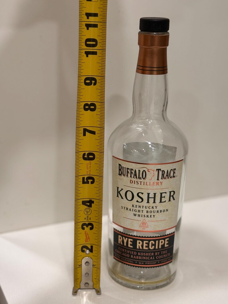 K&ouml;nnte beinhalten: Eine klare Glasflasche Buffalo Trace Kosher Kentucky Straight Bourbon Whiskey. Die Flasche ist etwa 25 cm hoch, mit einem schwarzen Verschluss und einer kupferfarbenen Halsmanschette. Das Etikett lautet "Rye Recipe".