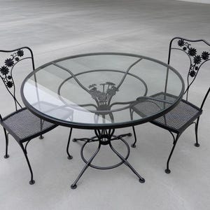 May include: A black metal patio set with a round glass table and two matching chairs. The chairs and table base have decorative floral accents. The table is approximately 36 inches in diameter.