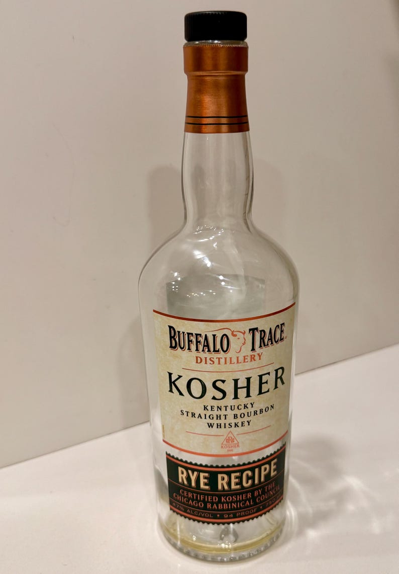 K&ouml;nnte beinhalten: Klare Glasflasche Buffalo Trace Kosher Kentucky Straight Bourbon Whiskey. Die Flasche hat einen schwarzen Verschluss und einen kupferfarbenen Hals. Das Etikett tr&auml;gt die Aufschrift "Rye Recipe" und "Certified Kosher by the Chicago Rabbinical Council."