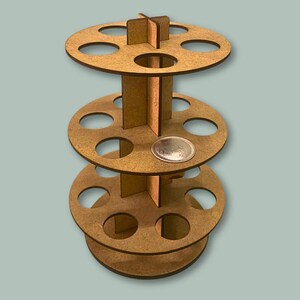 May include: A three-tiered wooden stand with circular shelves, each with multiple circular cutouts. The stand is made of light brown wood and has a silver metal dish on the middle shelf.