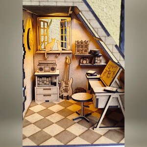 May include: A miniature wooden model of a room with a checkered floor, a window with two cats looking out, a guitar, a radio, a desk with a stool, and bookshelves with books and other objects.