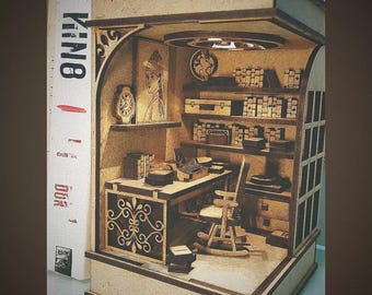Könnte beinhalten: Miniatur-Diorama aus Holz eines Schriftstellerbüros, mit Schreibtisch, Schreibmaschine, Bücherregalen und dekorativen Elementen. Das detaillierte Innere umfasst einen Schaukelstuhl und Kunstwerke.
