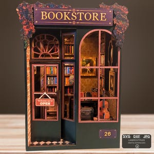 Puede incluir: Modelo de librería en miniatura con fachada verde oscuro y letrero morado que dice "BOOKSTORE". El modelo presenta ventanas abiertas que revelan estanterías, obras de arte y un violín. Un letrero en la puerta dice "Welcome we're OPEN."