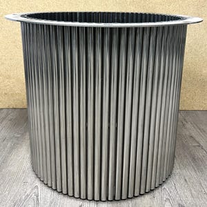 May include: A silver metal cylindrical container with a ribbed design. The container has a smooth top and bottom edge.
