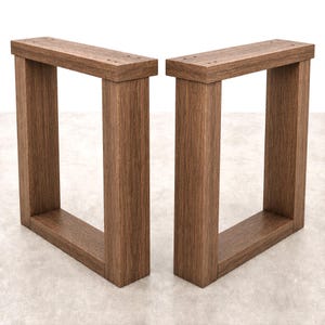 May include: A pair of rectangular furniture legs constructed from brown wood with a visible grain pattern. Each leg features a U-shaped frame design with a flat top bar containing pre-drilled holes for mounting purposes and two vertical supports.