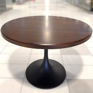 May include: A round wooden table with a dark brown top and a black pedestal base. The table is made of solid wood and has a smooth, polished finish.