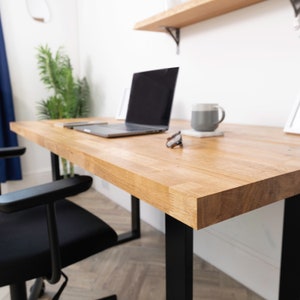 Pu&ograve; includere: Una scrivania in legno chiaro con gambe in metallo nero. Un computer portatile, una tazza e degli occhiali sono sulla scrivania.
