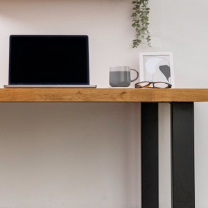 Pu&ograve; includere: Una scrivania in legno con gambe in metallo nero. Un computer portatile, una tazza grigia e un paio di occhiali sono sulla scrivania.