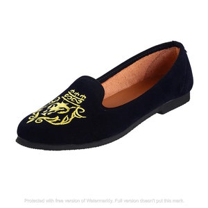 May include: Navy blue velvet flats with a gold embroidered design featuring a crown and a stylized animal.