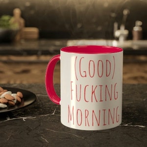 Puede incluir: Taza de café de cerámica blanca con borde y asa rojos. La taza tiene el texto "(GOOD)  FUCKING MORNING" impreso en rojo.
