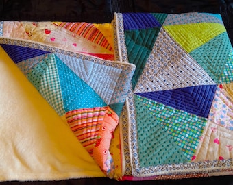 Könnte beinhalten: Eine bunte Patchwork-Decke mit verschiedenen Stoffen, darunter Blau, Grün, Gelb und Rosa. Die Decke ist in der Mitte gefaltet und hat eine weiße Rückseite.