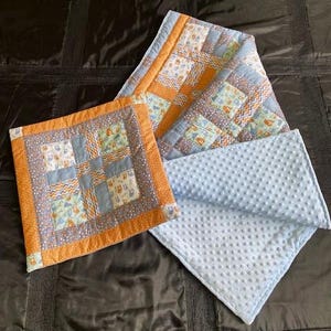 Könnte beinhalten: Eine blaue und orangefarbene Patchwork-Babydecke mit weichem, blauem Minky-Rücken. Die Decke besteht aus verschiedenen Stoffen mit unterschiedlichen Mustern, darunter Eulen, geometrische Formen und Zickzackmuster.